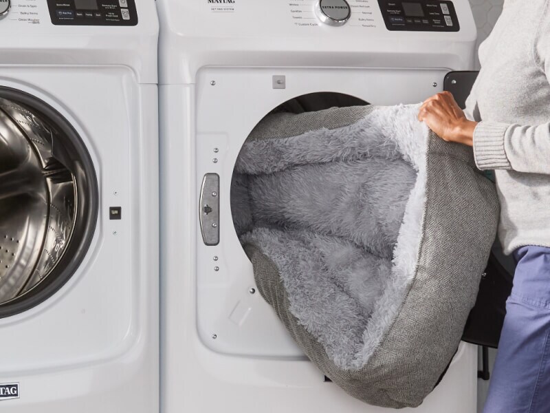A person loading a dog bed into a dryer