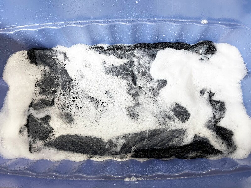 A dog bed submerged in a basin filled with water and pet-safe detergent