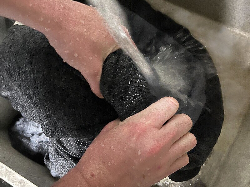 A person rinsing a dog bed under running water