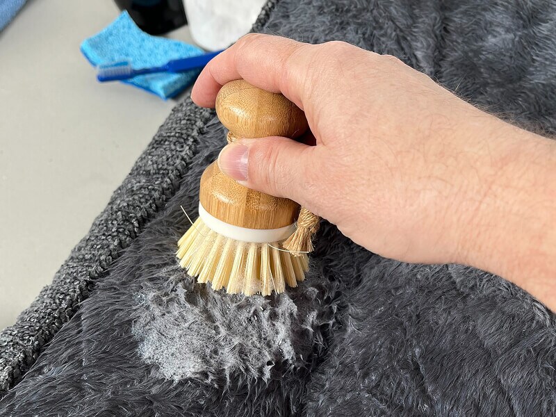 A person scrubbing a stain on a dog bed with a scrub brush