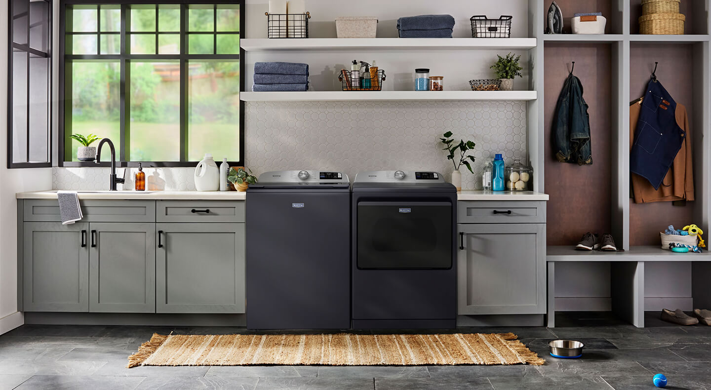 A washer and dryer in a laundry room and an empty metal dog bowl