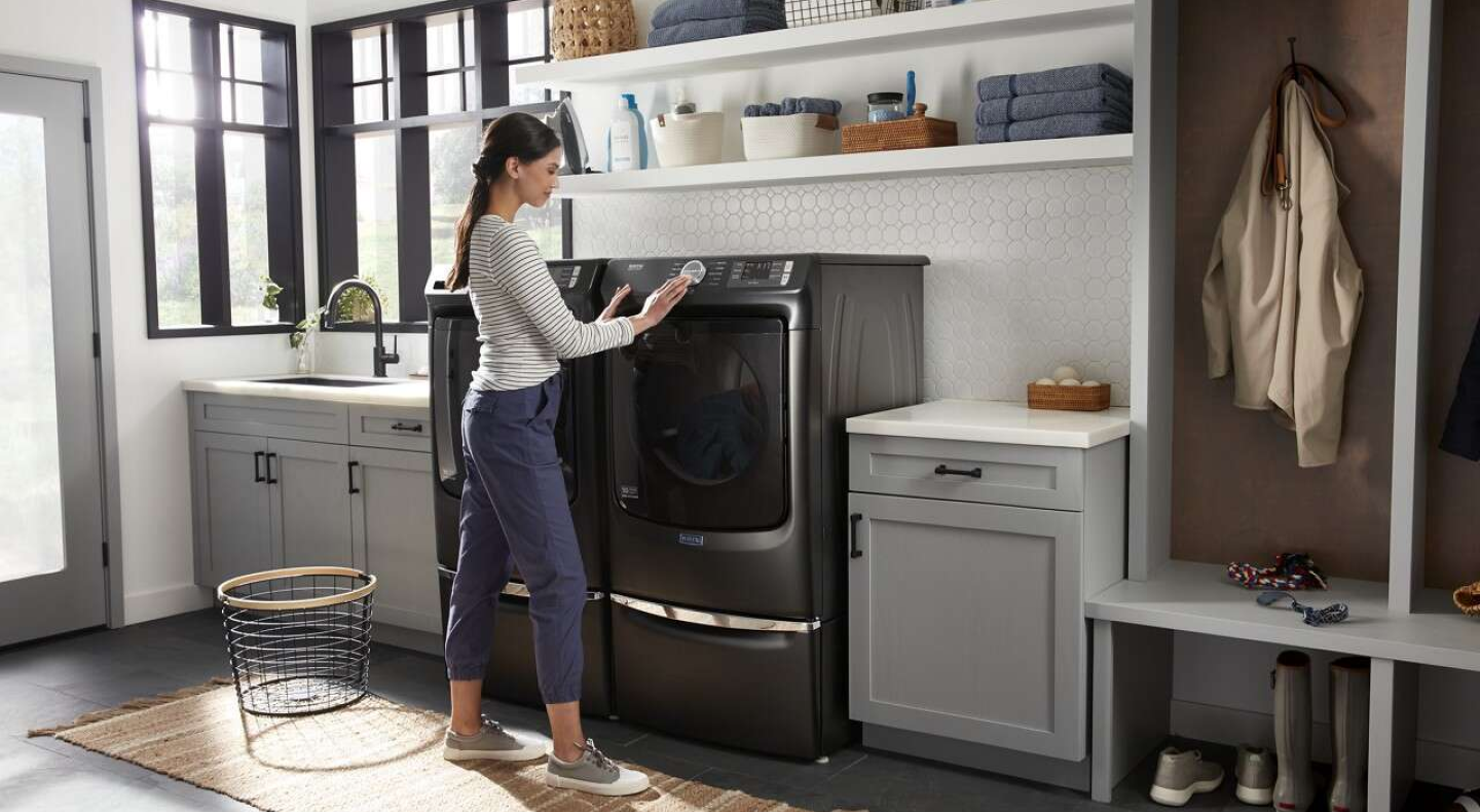 A woman programming a Maytag® dryer setting in a modern laundry room.