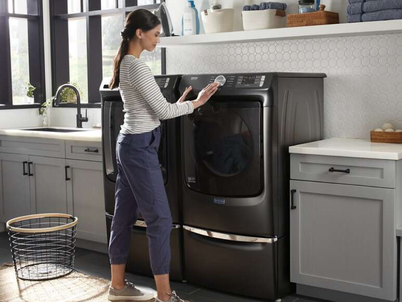 A woman programming a Maytag® dryer setting in a modern laundry room. A woman programming a Maytag® dryer setting in a modern laundry room.