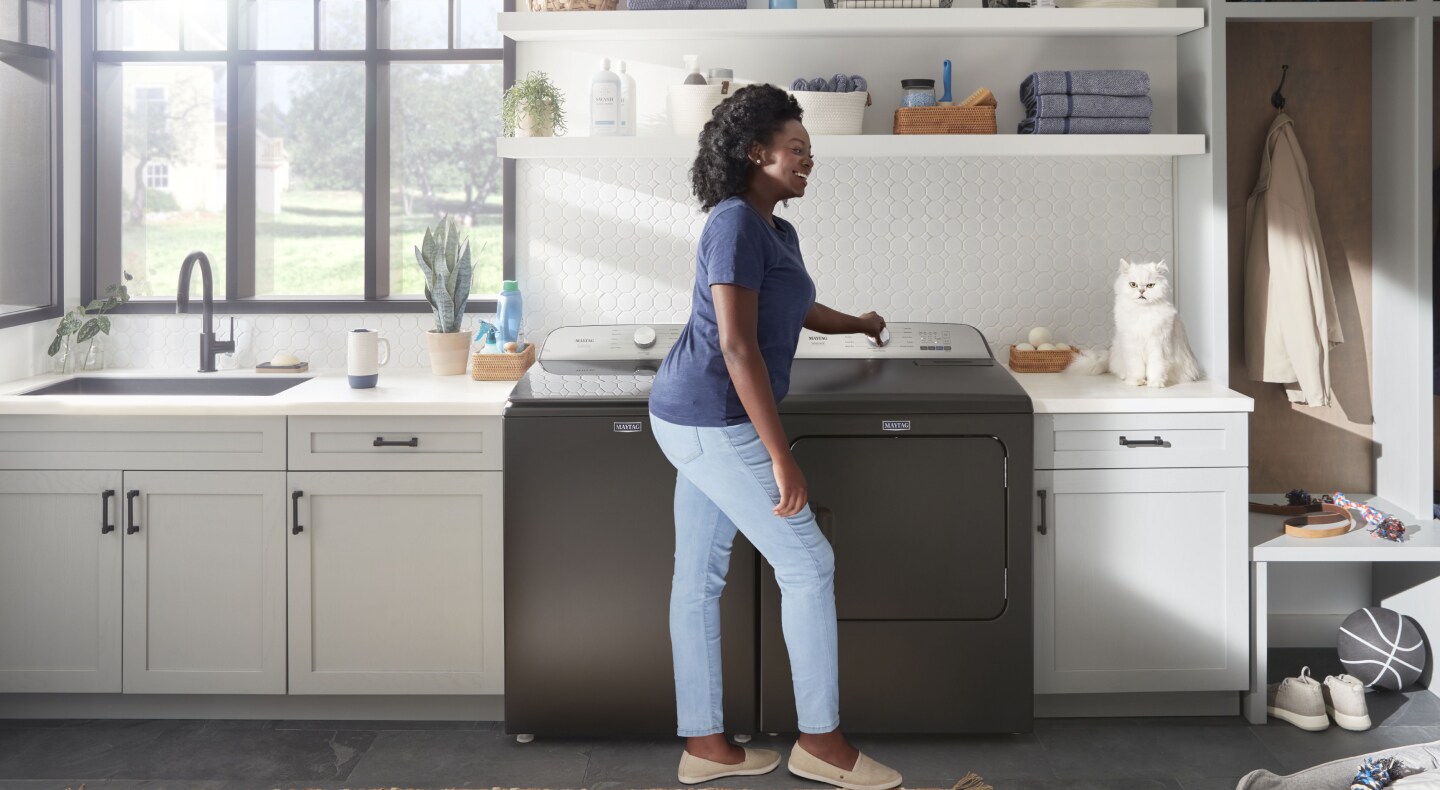 Person turning Maytag® dryer knob and smiling at their pet cat. Person turning Maytag® dryer knob and smiling at their pet cat.