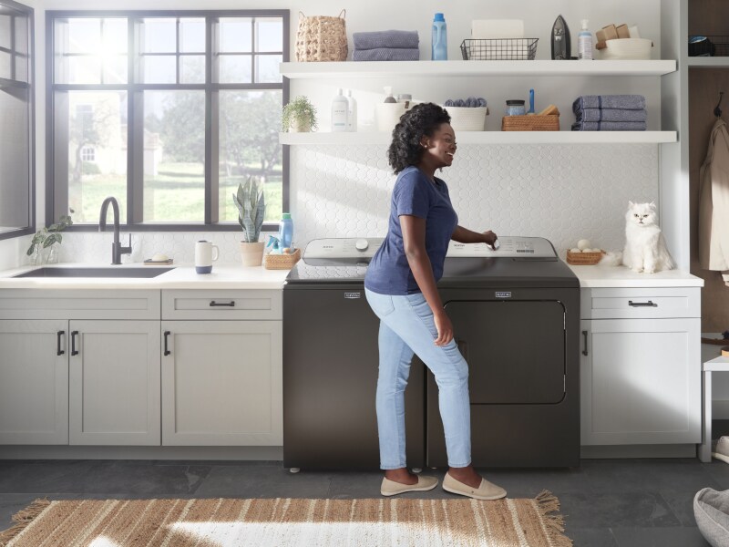 Person turning Maytag® dryer knob and smiling at their pet cat. Person turning Maytag® dryer knob and smiling at their pet cat.