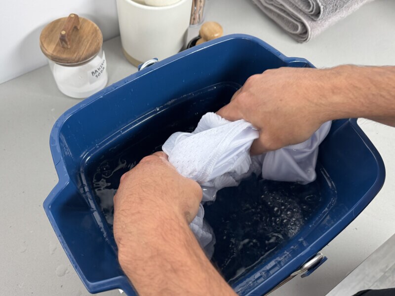 Two hands squeezing out a jersey that has been soaking in water and vinegar