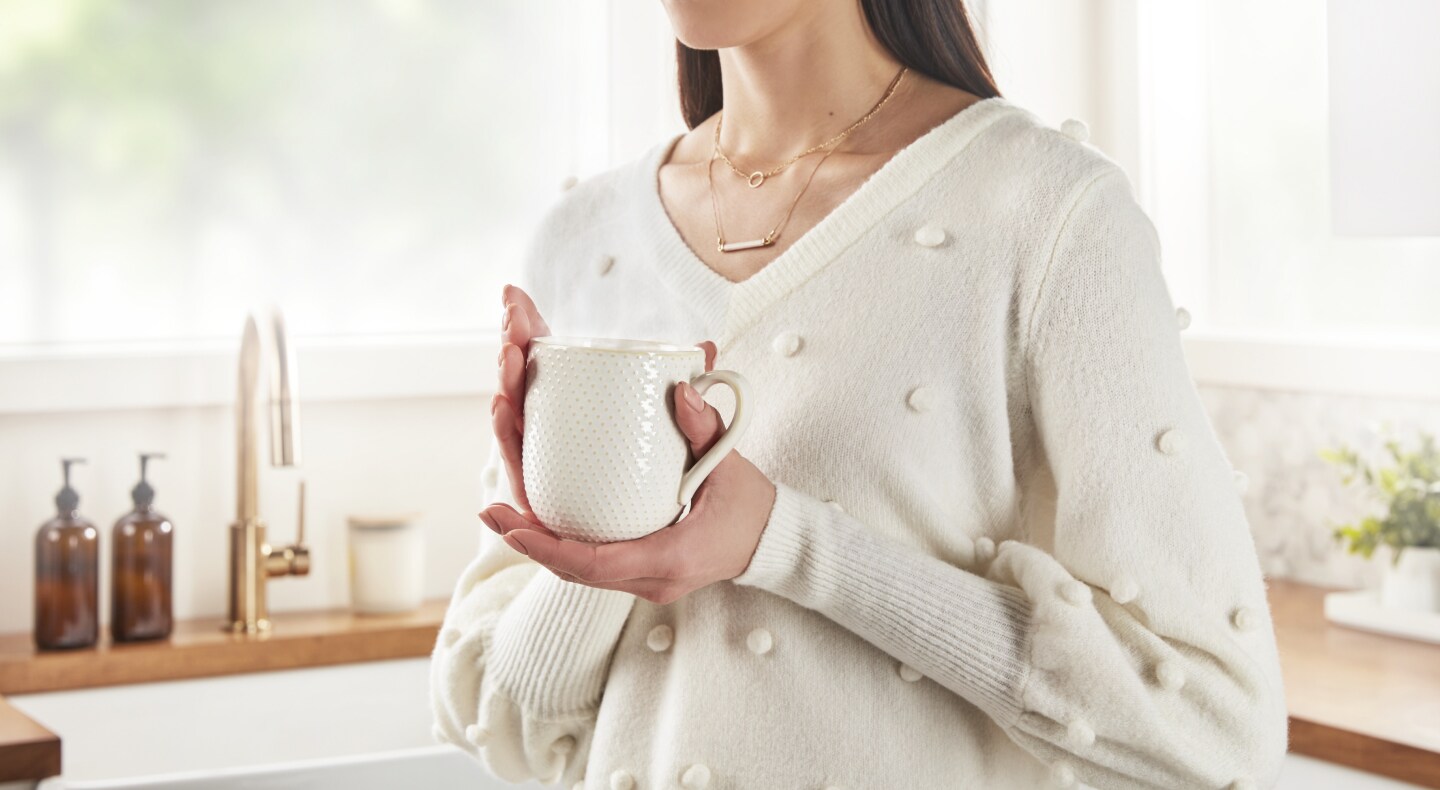 A person wearing a hand-knitted shirt, holding a mug