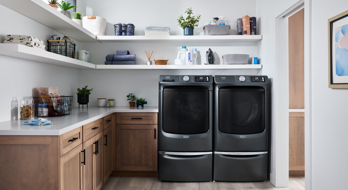 A front load washer and dryer pair in a laundry area with white, open shelving