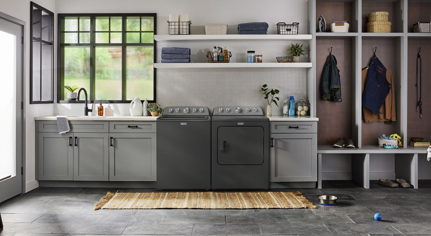 A laundry area with a top load washer and dryer set surrounded with grey cabinetry and open shelving above
