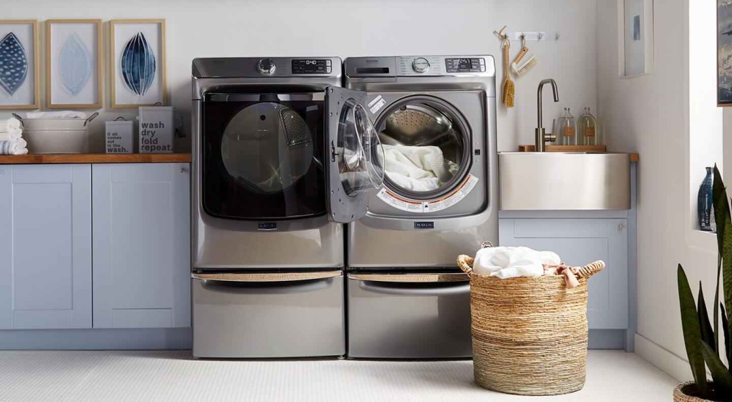 A sliver washer and dryer pair in a bright laundry room with blue cabinetry