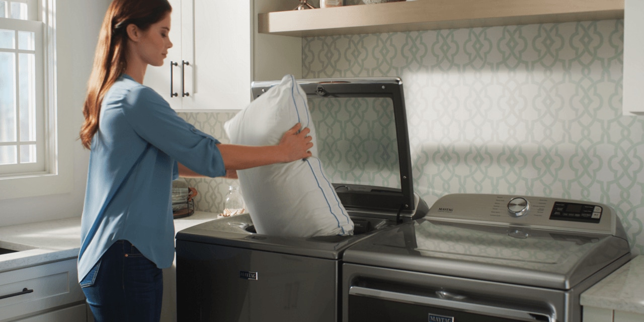 Woman loading a pillow into a Maytag® top loading washer Woman loading a pillow into a Maytag® top loading washer