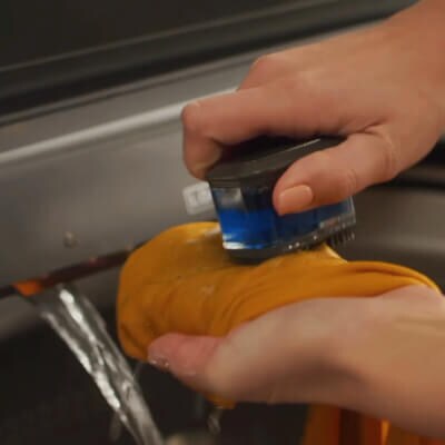 Person using scrub brush to pretreat stains under built-in water faucet in washer