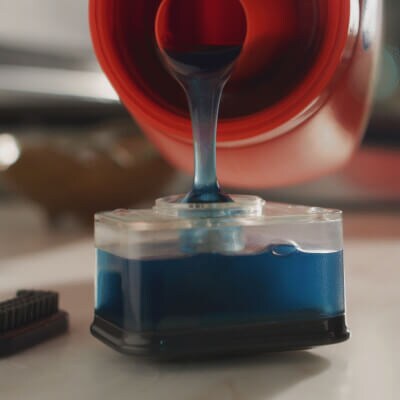 Person pouring detergent into the compartment of a scrub brush