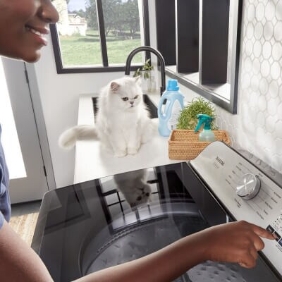 Person selecting settings on washer with a white cat in the background