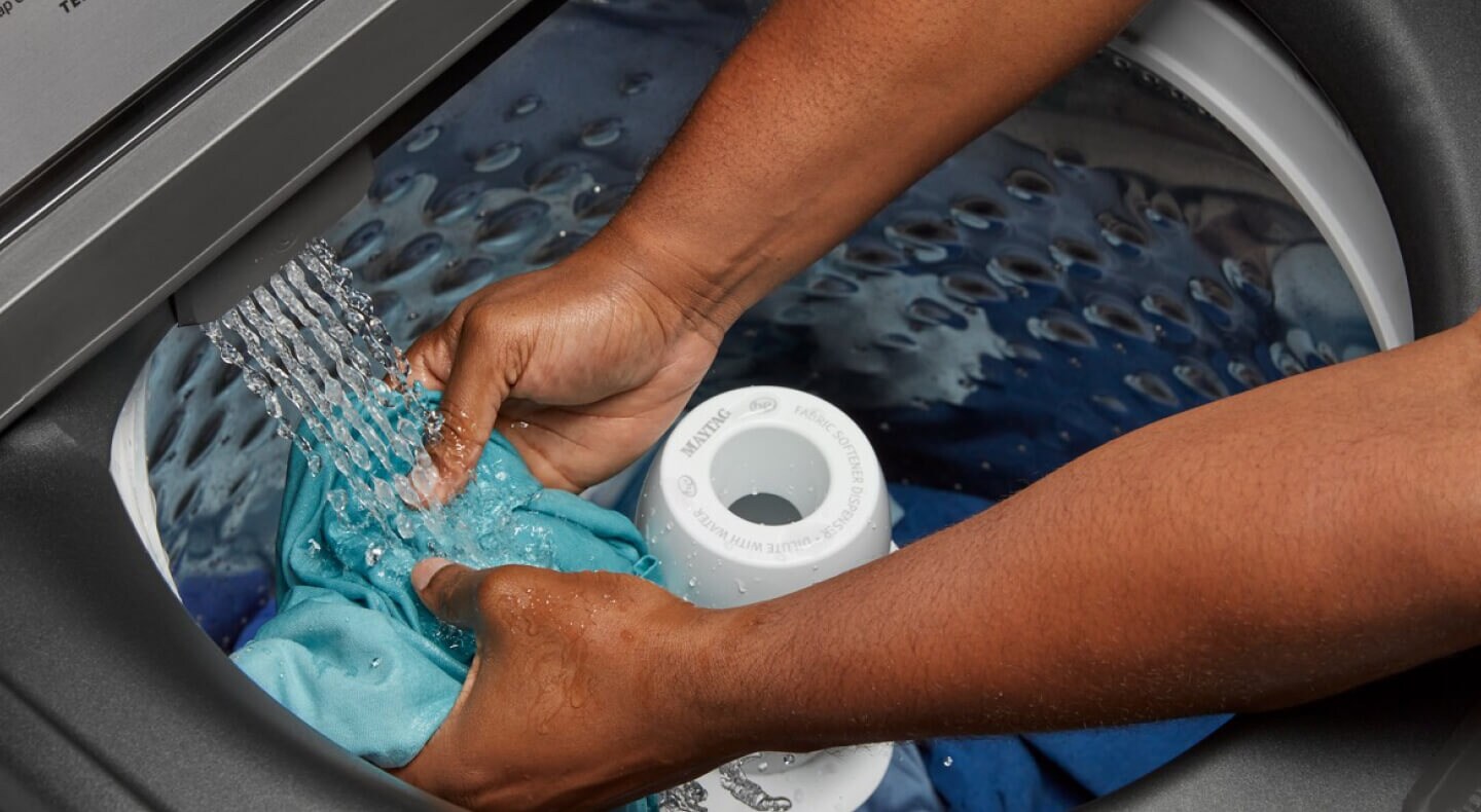 Close-up of a person pretreating stains on a blue shirt in a Maytag® top-load washer