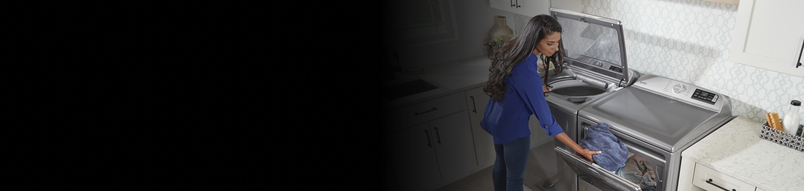 Person transferring clothes from gray, top-load Maytag® washer to a matching dryer