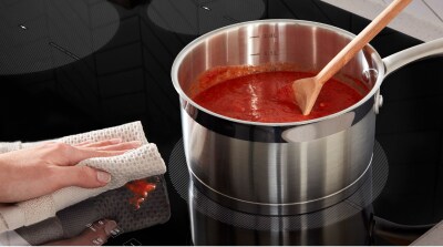 Red sauce in a pan on induction cooktop with a hand wiping a small splatter