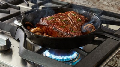 Steak and mushrooms in cast iron skillet on gas cooktop