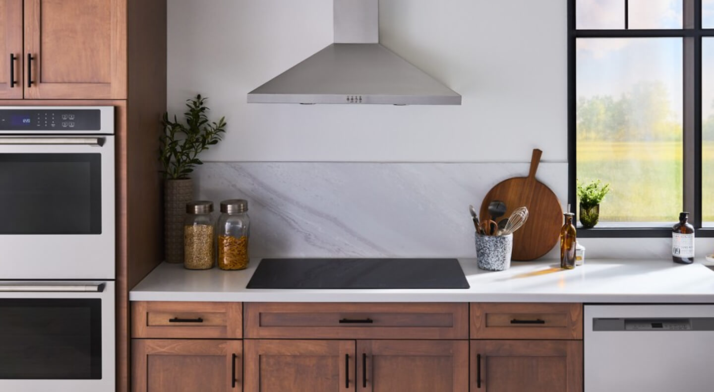 Induction cooktop in white countertop below wall mount range hood