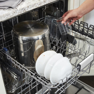 Person loading cups into the top rack of a dishwasher