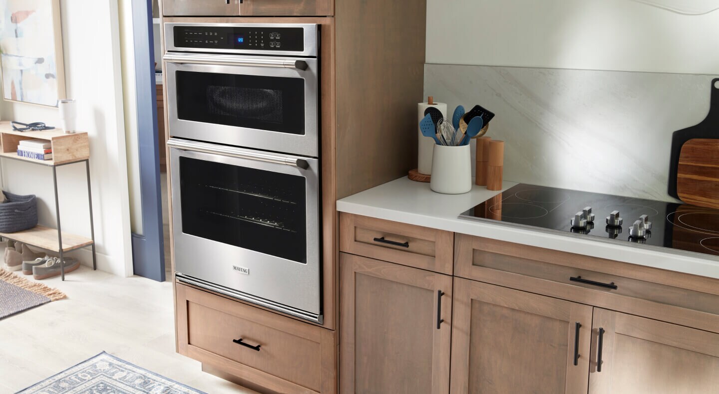  Maytag® wall oven microwave combo in brown cabinetry next to an electric cooktop