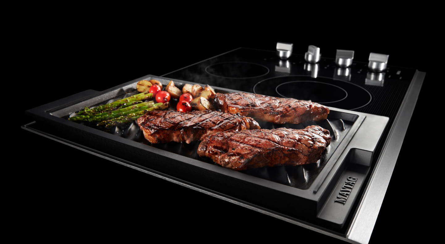 Steaks and veggies on a cooktop grill on top of an electric stovetop