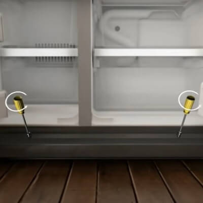 Close-up of the bottom of the fridge with screwdrivers removing grille plate