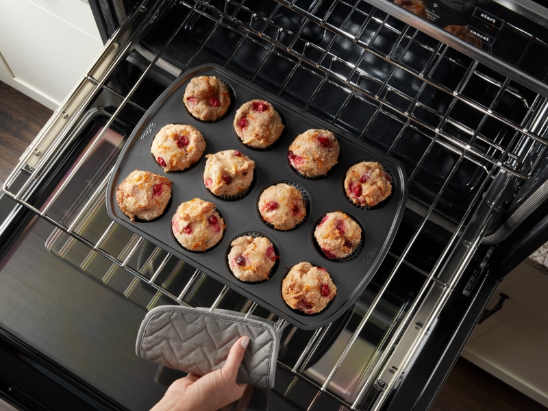 Birds-eye view of person using hot pad to remove muffins from the oven