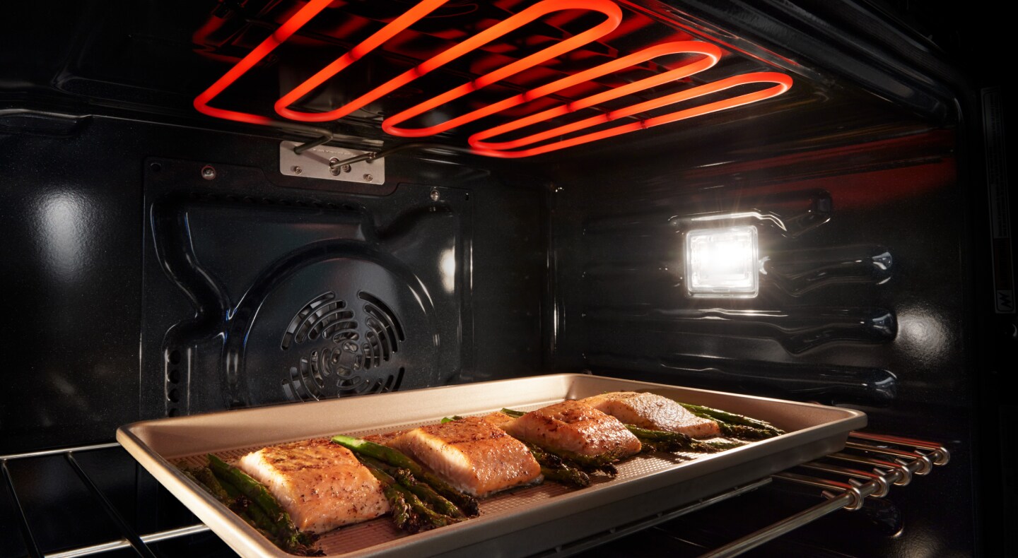 Salmon and asparagus roasting inside of oven cavity under heating element Salmon and asparagus roasting inside of oven cavity under heating element