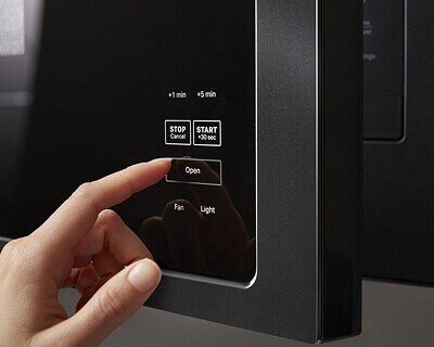 Person selecting button to open an over-the-range microwave
