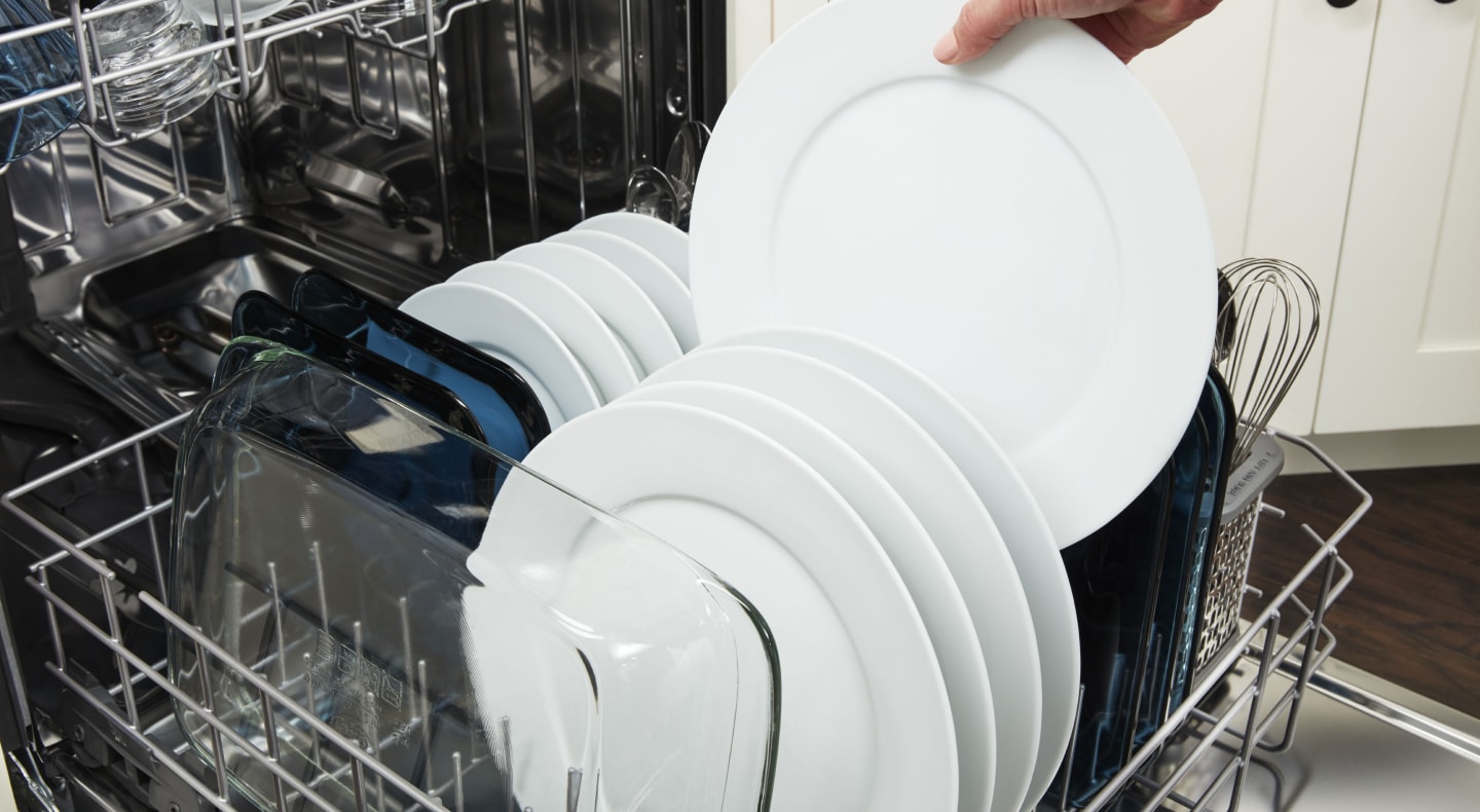 A person unloading a clean dish from a dishwasher rack  A person unloading a clean dish from a dishwasher rack