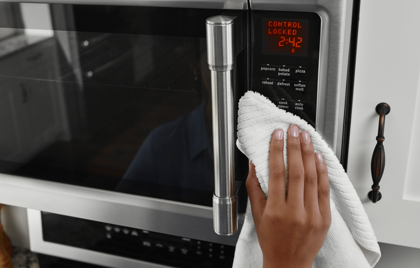 Hand holding white towel wiping microwave control panel Hand holding white towel wiping microwave control panel