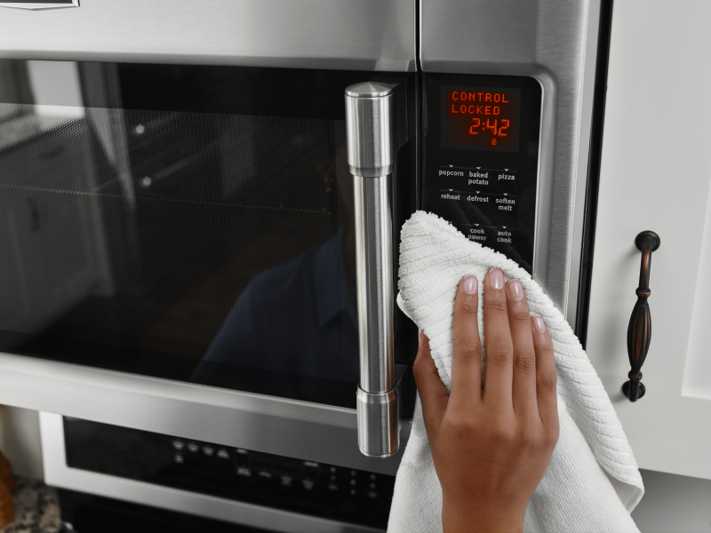 Hand holding white towel wiping microwave control panel Hand holding white towel wiping microwave control panel