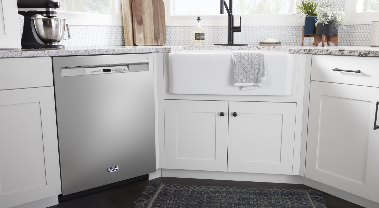 A stainless steel dishwasher with a pocket handle surrounded by white cabinets