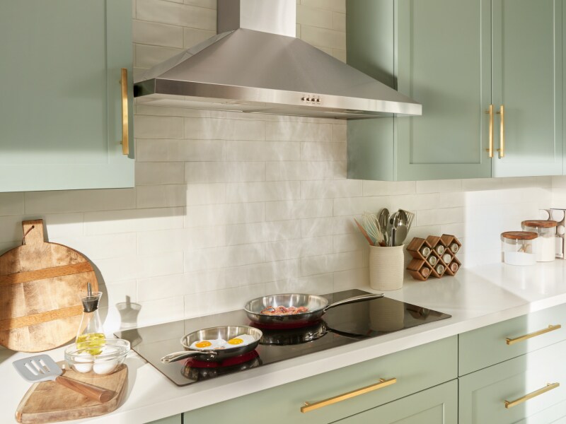 Eggs and bacon frying on a cooktop with a stainless steel range hood Eggs and bacon frying on a cooktop with a stainless steel range hood