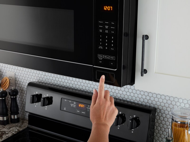 A person using a black over-the-range microwave A person using a black over-the-range microwave