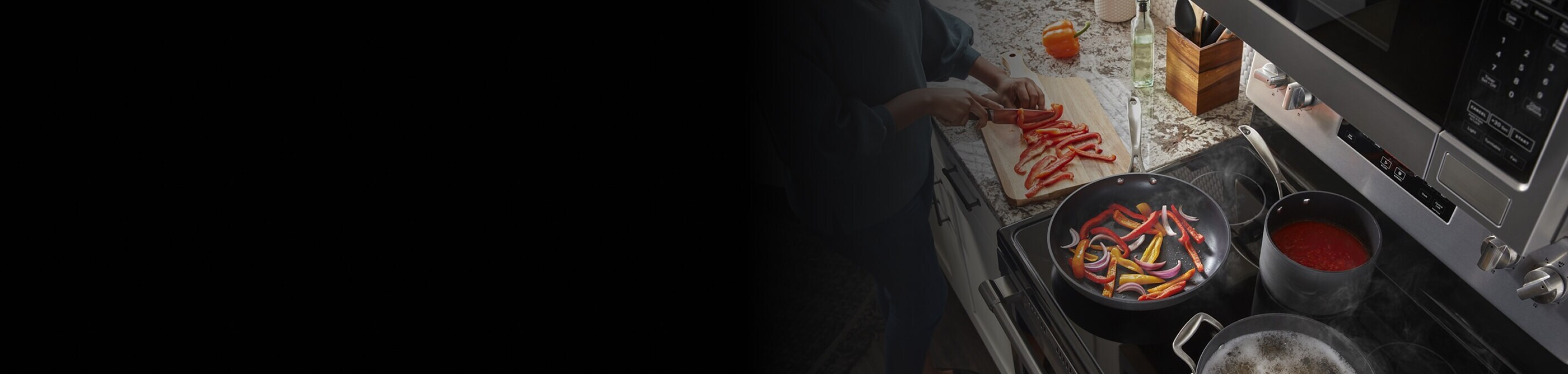 Woman chopping a red bell pepper on a wooden cutting board next to an electric range