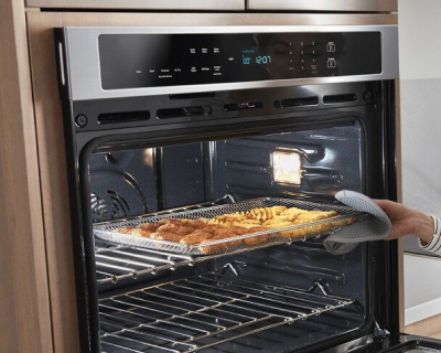 Hand holding an oven mitt sliding a baking sheet into the oven