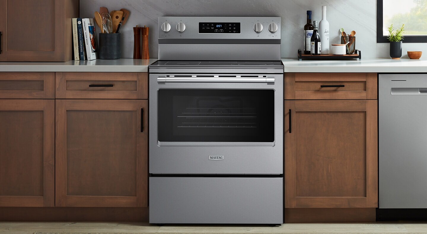 A Maytag® slide-in electric range in between wooden kitchen cabinets
