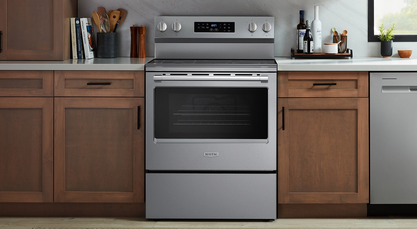 A Maytag® slide-in electric range in between wooden kitchen cabinets