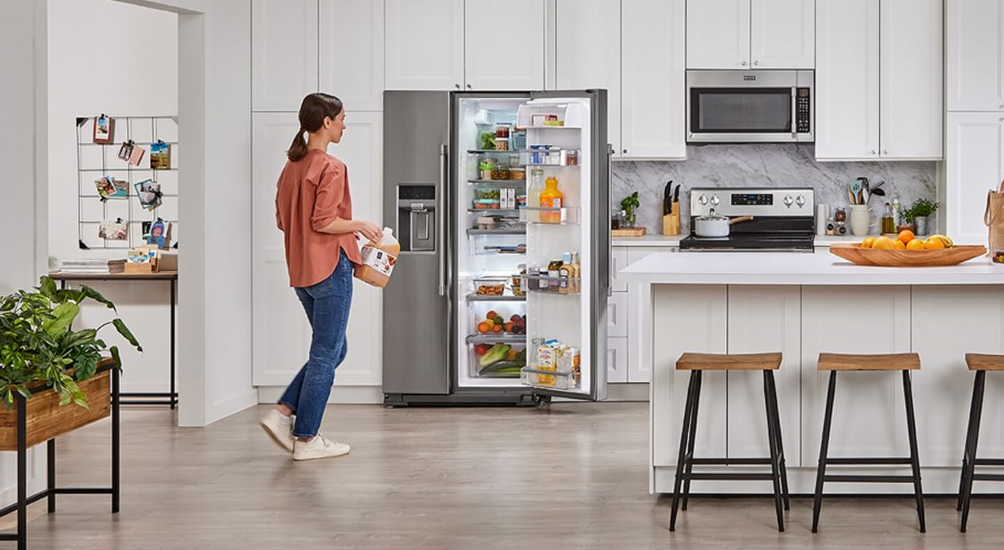 A large white kitchen with a person approaching a stainless steel side-by-side refrigerator