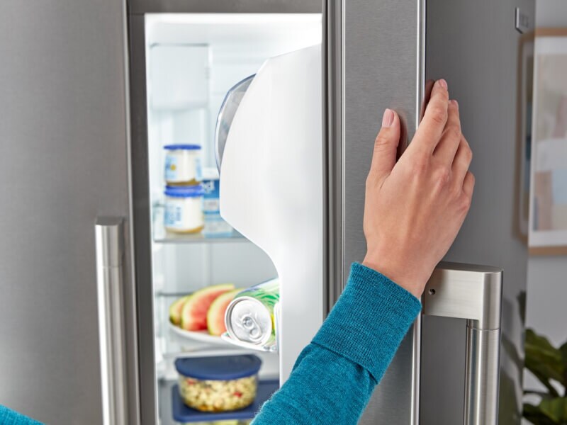 A hand on an open refrigerator door