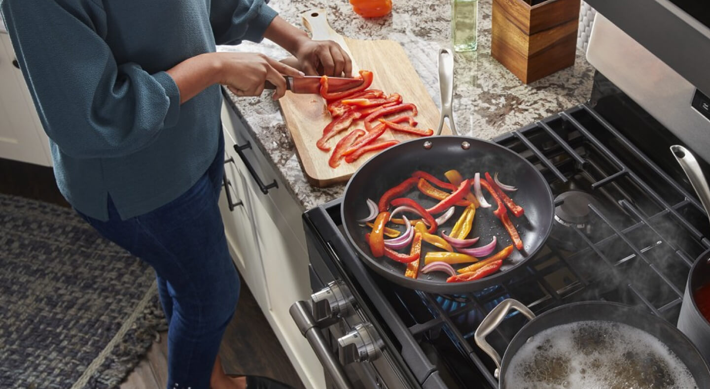 A person chopping vegetables near their range