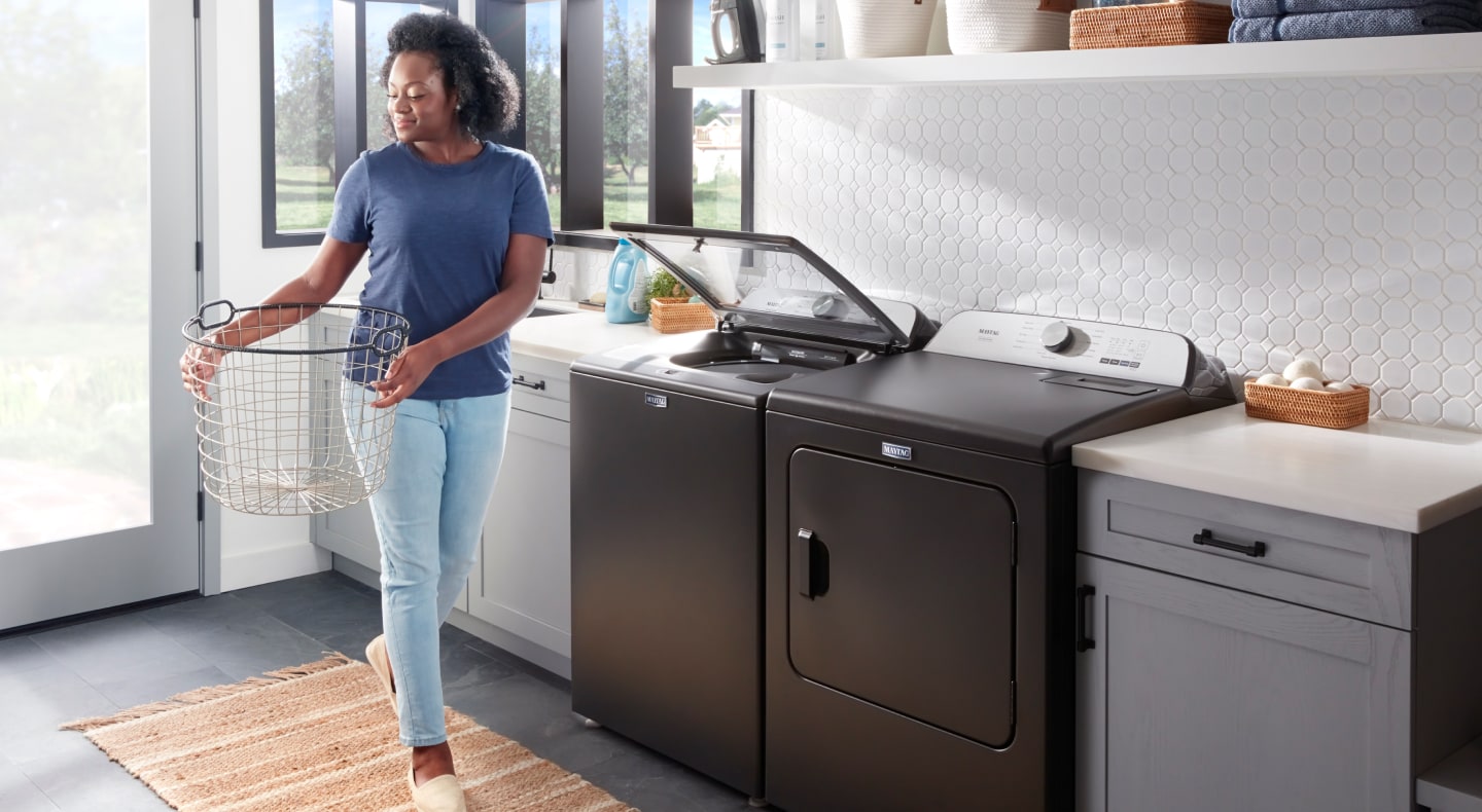 Person carrying a laundry basket next to a washing machine Person carrying a laundry basket next to a washing machine