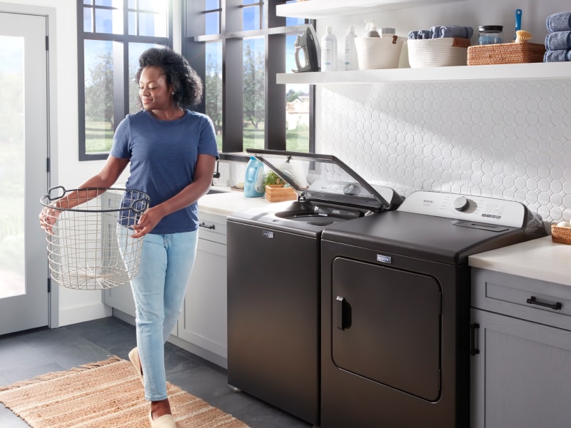 Person carrying a laundry basket next to a washing machine Person carrying a laundry basket next to a washing machine