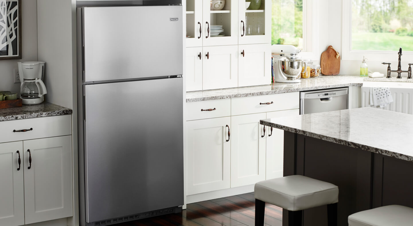 Stainless steel top freezer refrigerator in a kitchen with white cabinetry and grey granite countertops