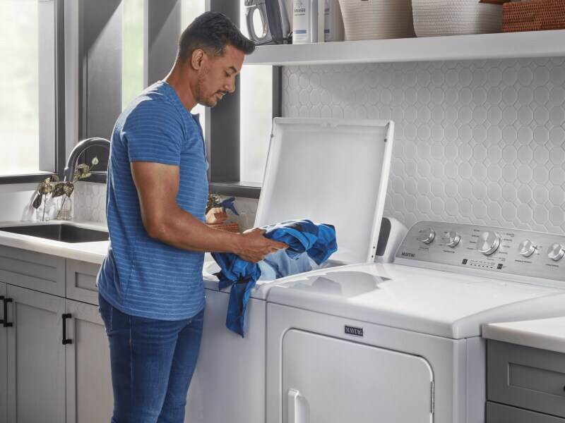 Person loading clothes into a white Maytag® top load washer 