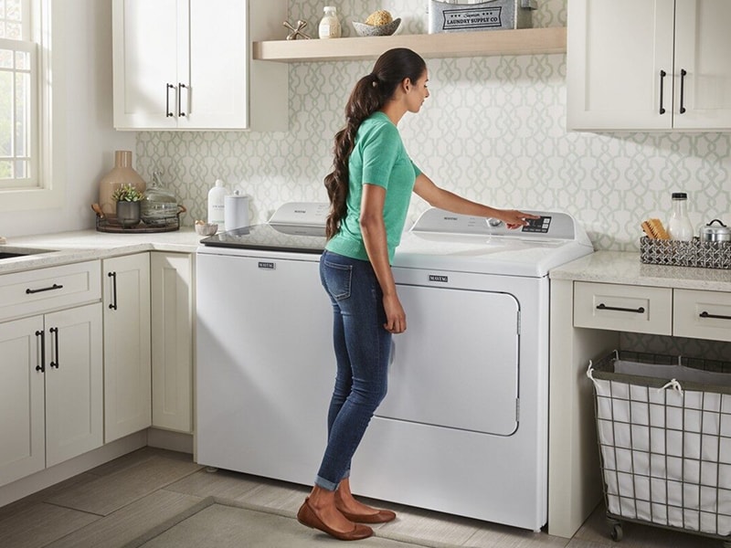 Person selecting option on a dryer in a white laundry room