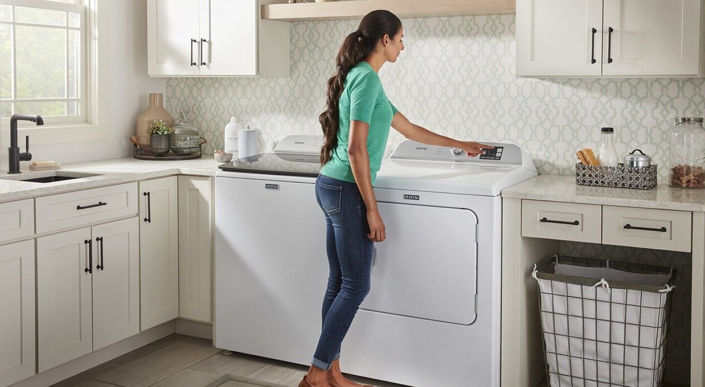 Person selecting option on a dryer in a white laundry room