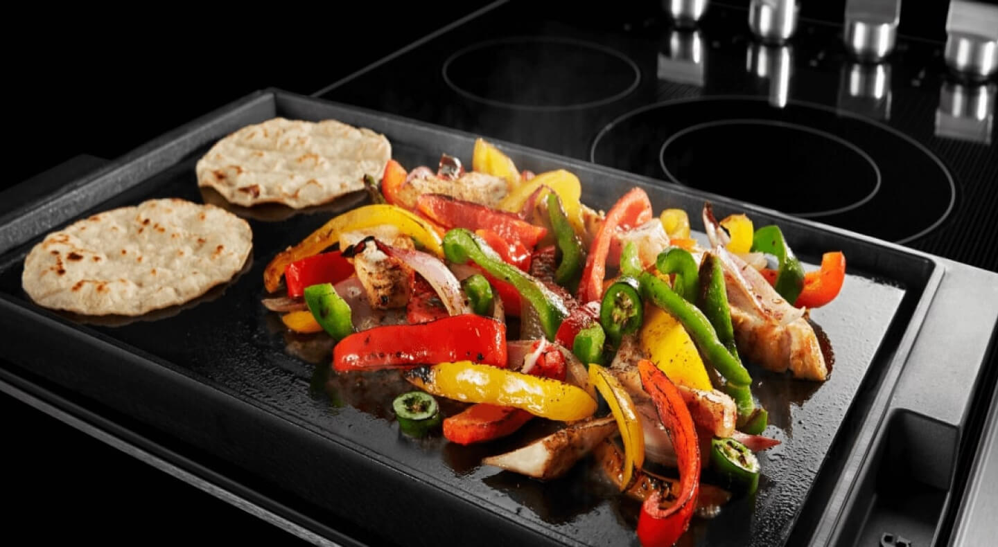 Fajitas cooking on an electric cooktop with a griddle